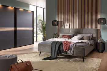 Graues Polsterbett mit schwarzen Beinen in einem modernen Raum mit Paneelwand.